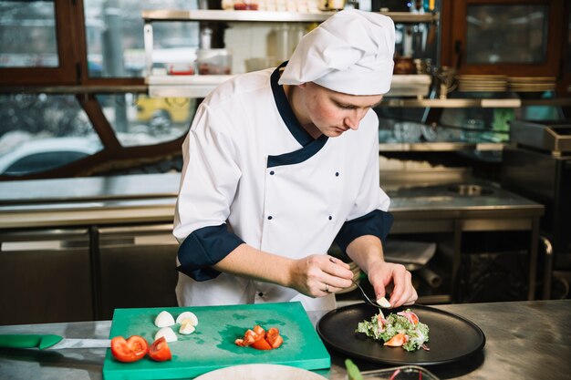 Cook putting boiled egg on plate with salad