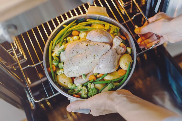 Cook putting raw chicken to the oven 