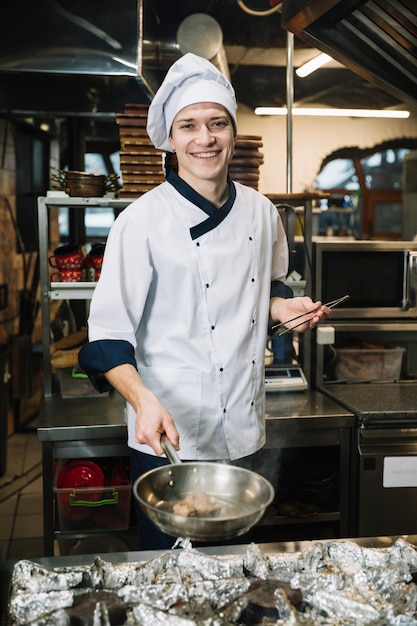 Cook standing with fried meat in pan 