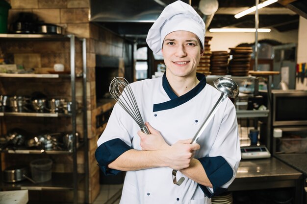 Cook standing with whisk and ladle in kitchen