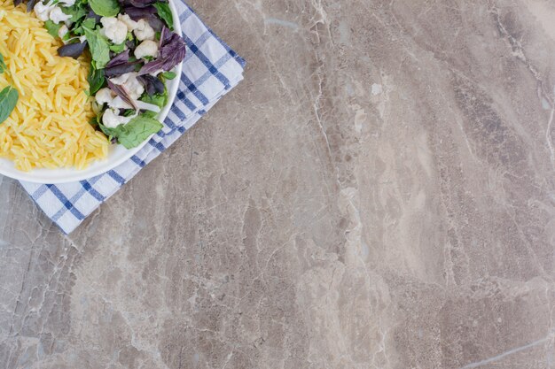 Riso integrale cotto con insalata appetitosa su un piatto su marmo.