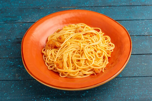 приготовленная итальянская паста вкусная внутри оранжевой тарелки на синем дереве