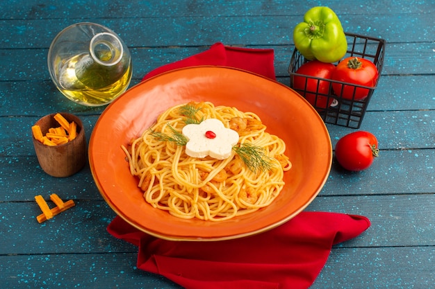 cooked italian pasta with greens inside orange plate with oil and vegetables on blue wood