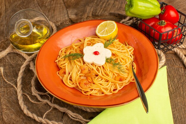 나무에 주황색 접시 안에 야채와 기름과 함께 채소와 레몬 조각으로 요리 한 이탈리아 파스타