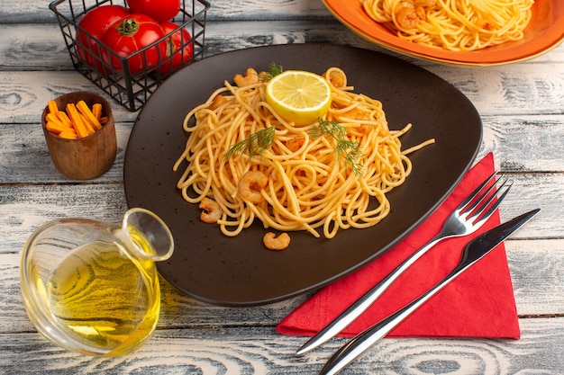 приготовленная итальянская паста с креветками, зеленью и лимоном внутри коричневой тарелки на сером