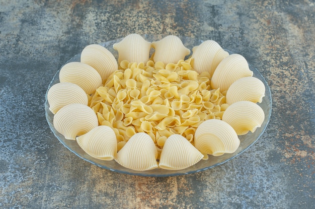 Cooked pipe and uncooked bow tie pastas in the bowl, on the marble background.