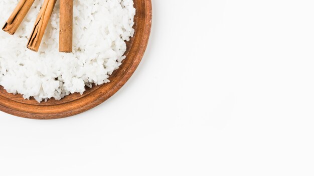 Cooked rice with cinnamon sticks on wooden plate against white background