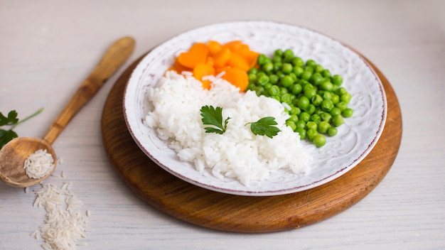 Cooked rice with vegetables on wooden board near spoon