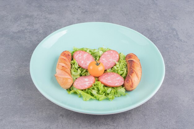 Cooked sausage and sliced sausage on the plate, on the marble surface