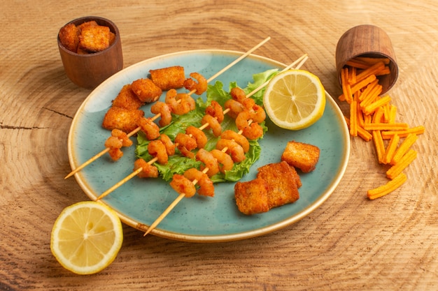 Free photo cooked shrimps on sticks inside blue plate with green salad and lemon slices on wooden desk