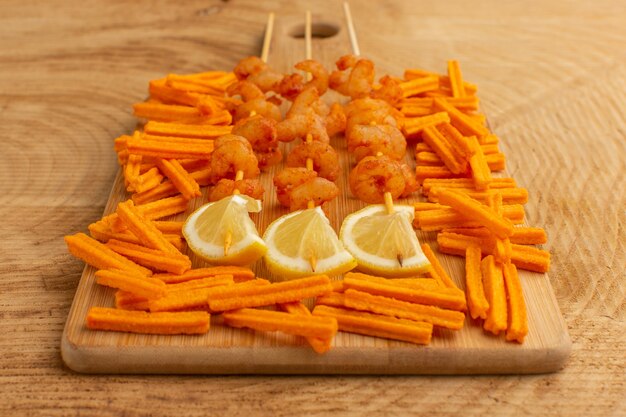 cooked shrimps on sticks with lemon slices and rusks on wooden desk