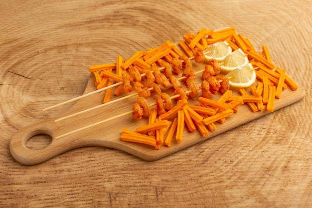 cooked shrimps on sticks with lemon slices and rusks on wooden desk