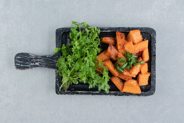 Cooked sliced pumpkin next to parsley, on the tray , on the marble background.