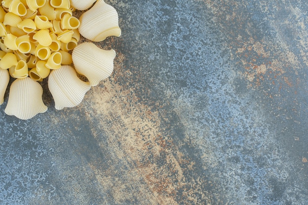 Cooked and uncooked pastas in the bowl, on the marble background.