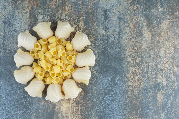 Cooked and uncooked pastas in the bowl, on the marble surface.