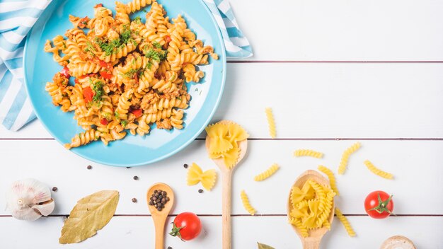Cooked vegetable pasta fusilli with ingredients on white wooden backdrop