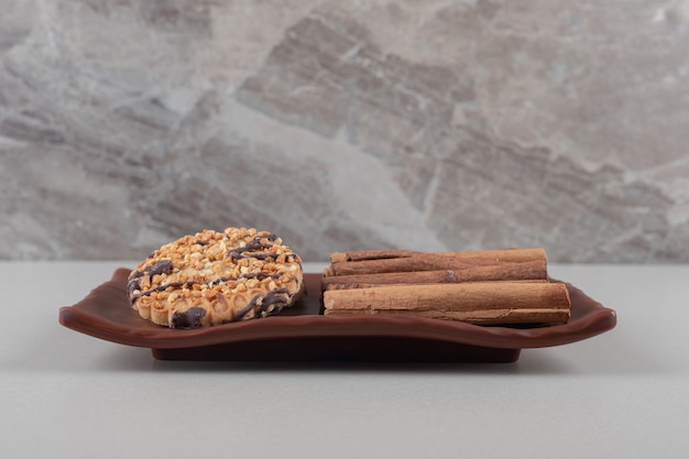 cookie and a bundle of cinnamon sticks on a platter on marble background.