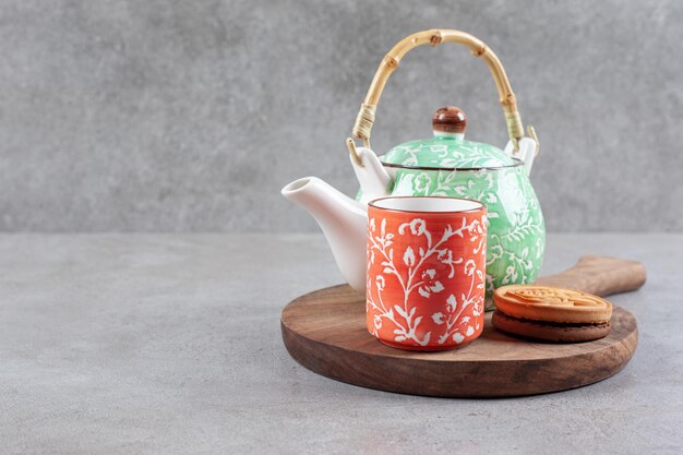 A cookie, a cup of tea and a teapot on wooden board on marble background. High quality photo