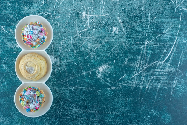 Печенье и кексы в небольшом сервировочном блюде на синем фоне. Фото высокого качества