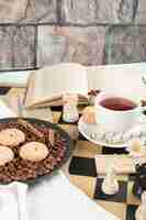 Free photo cookie platter and a cup of tea on the chessboard