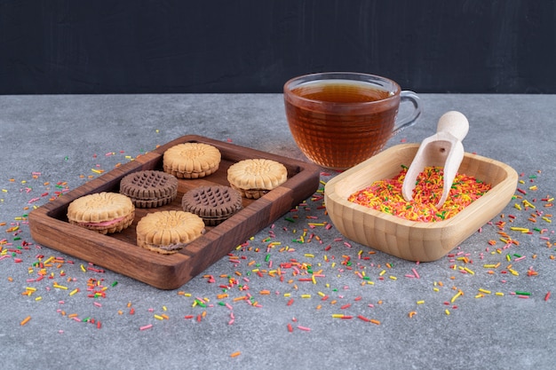Cookies, a bowl of candy sprinkles and a cup of tea 