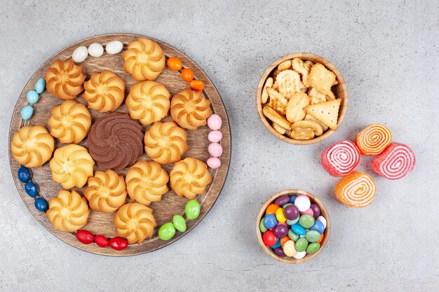 Cookies and candies on wooden board and in wooden bowls with marmelades on marble background. High quality photo