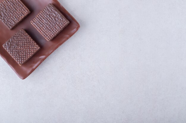 Cookies and chocolate wafers on wooden plate on marble table.