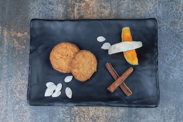 Free photo cookies, cinnamon and slices of pumpkin on black plate. high quality photo