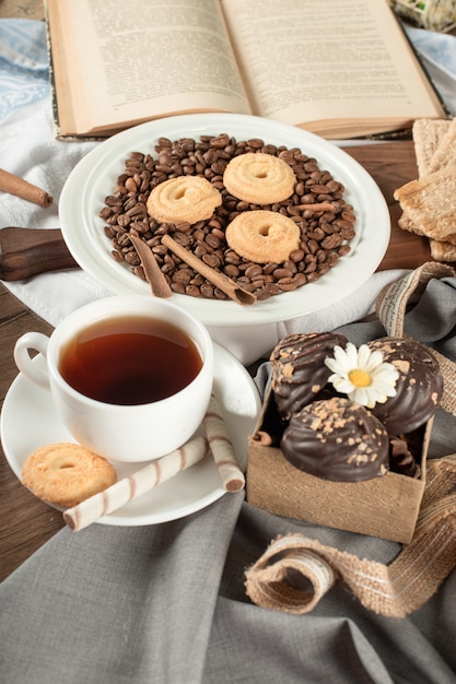 Cookies on coffee beans in a saucer and a cup of tea.