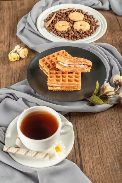 Cookies on coffee beans with waffler in a saucer and a cup of tea.