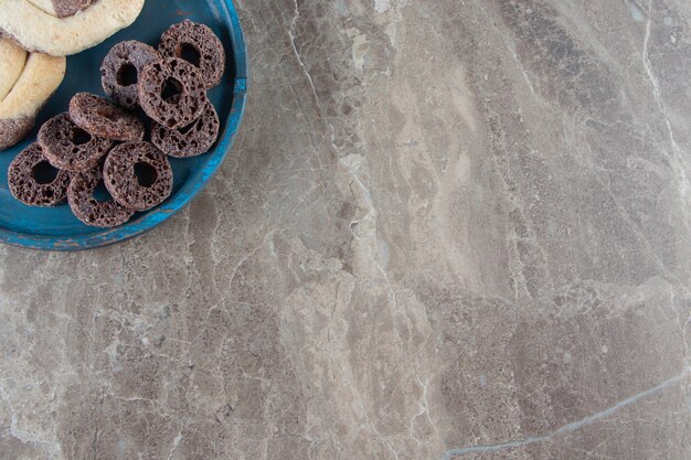 Cookies and corn rings on a wooden plate on marble.