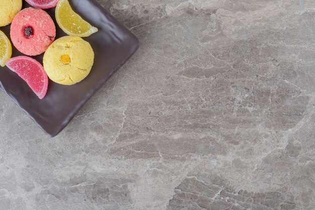 Cookies and jelly sweets bundled on a platter on marble surface