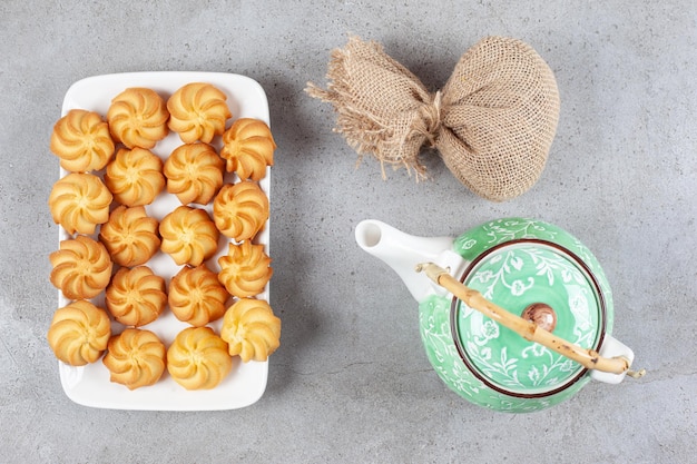 Free photo cookies lined up on a platter next to a sack and a teapot on marble surface