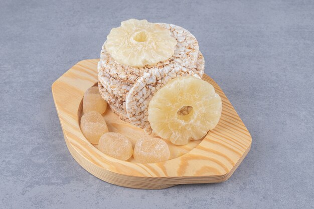Cookies, marmelades and dried pineapple slices on a wooden platter on marble