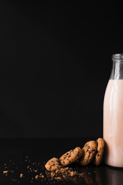 Cookies near the milk bottle against black background