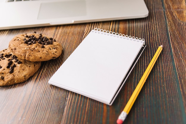 Cookies near notebook with pencil and laptop