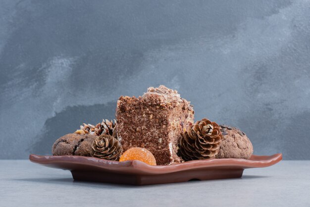 Cookies, pine cones, jelly candies and a slice of cake on a platter on marble surface