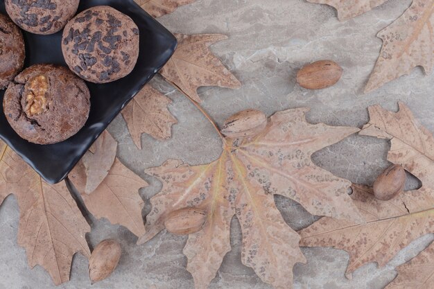 散らばったプラタナスの葉の横にある大皿のクッキーと大理石のピーカンナッツ