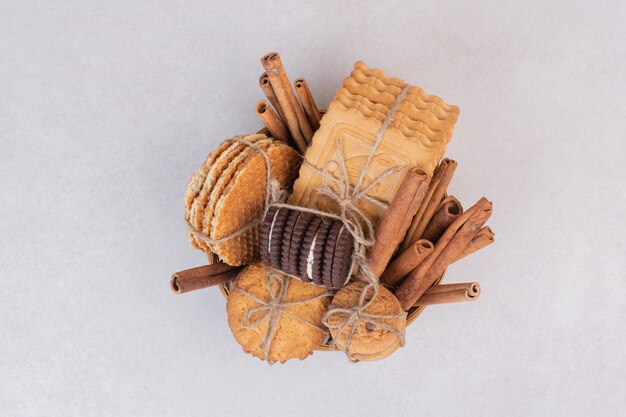 Cookies in rope with cinnamon sticks on white surface