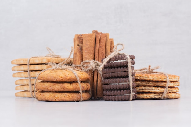 Cookies in rope with cinnamon sticks on white table.