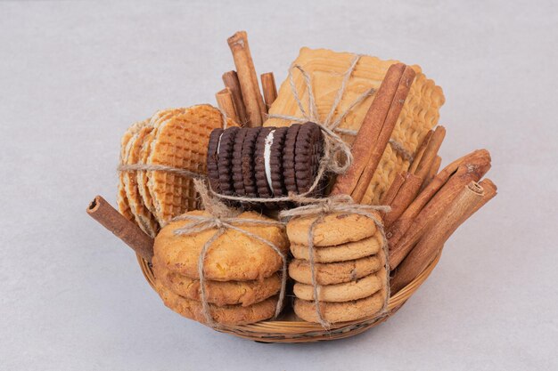 Cookies in rope with cinnamon sticks on white table.