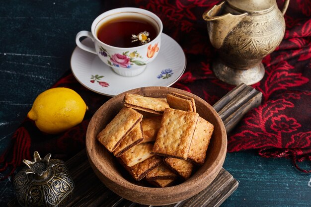 Cookies with cocoa filling in a wooden cup with a cup of tea.