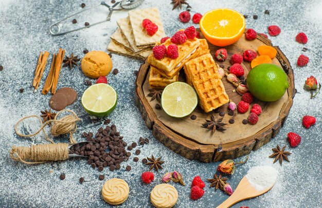 Cookies with flour, herbs, fruits, spices, choco, strainer flat lay on wooden board and stucco background