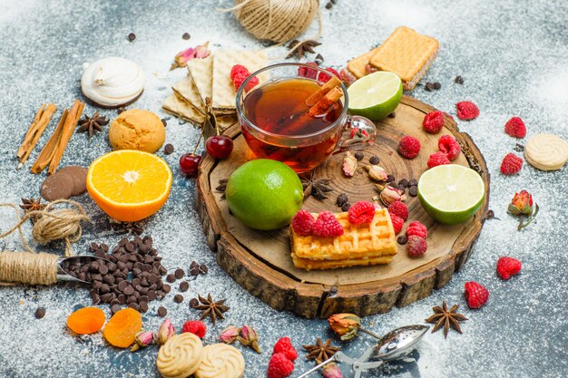 Cookies with flour, tea, fruits, spices, choco high angle view on wooden board and stucco background