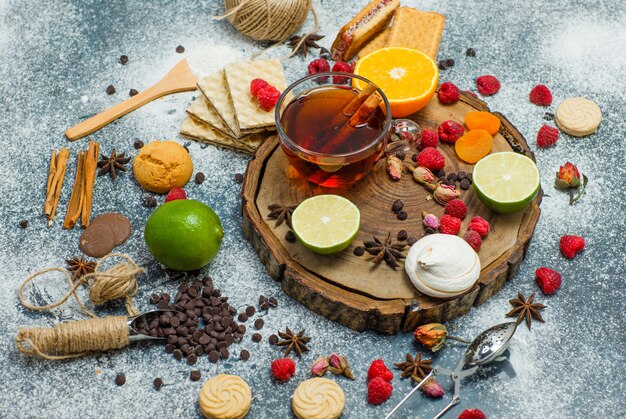 Cookies with flour, tea, fruits, spices, choco, strainer flat lay on wooden board and stucco background