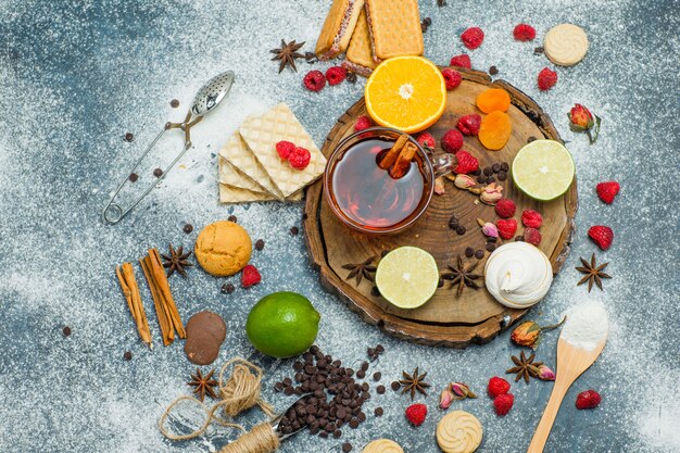 Cookies with flour, tea, fruits, spices, choco, strainer on wooden board and stucco background, top view.