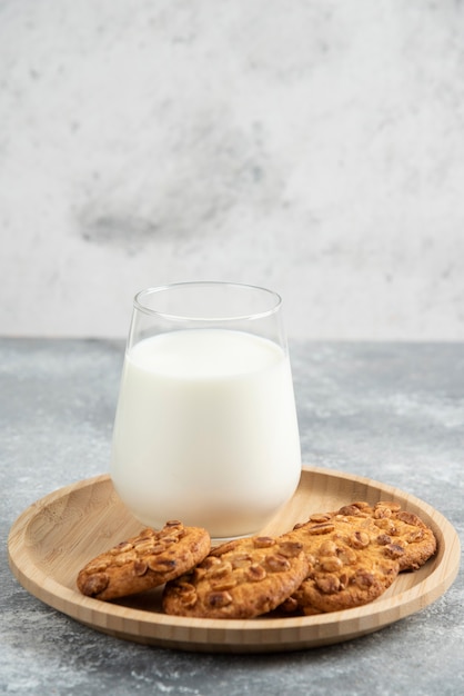 Cookies with organic peanuts and glass of milk on wooden plate. 