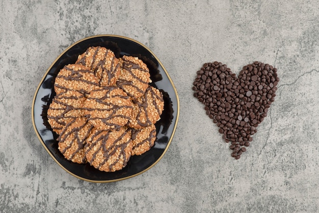 Cookies with seeds on black plate with pile of drop chocolate.