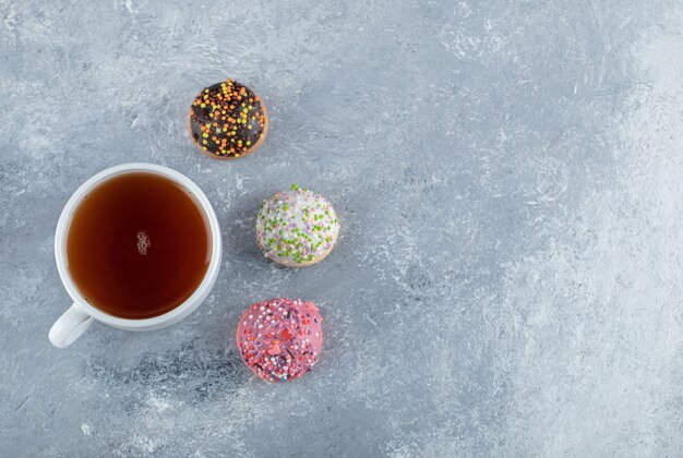 Cookies with sprinkles and cup of tea on marble table. 