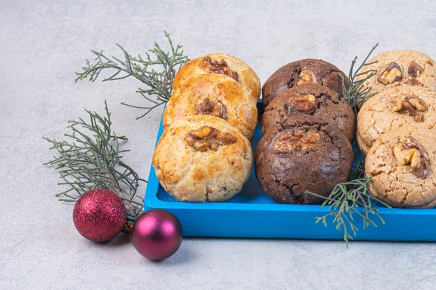 Cookies with walnut on a board next to baubles and brunch, on the marble.